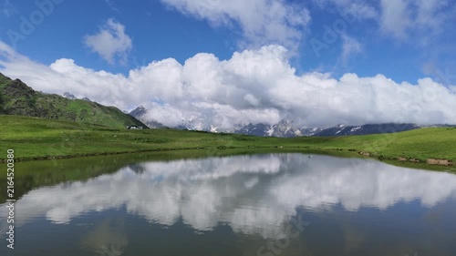 Pristine mountain lake reflecting puffy white clouds and blue sky, green alpine meadows at Koruldi lakes in Svaneti region of Georgia, perfect for travel or nature background