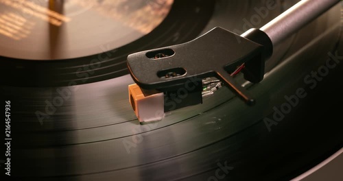 Detailed close-up of a turntable tonearm with white cartridge headshell, positioned over a black vinyl record on the platter, highlighting audio equipment precision.