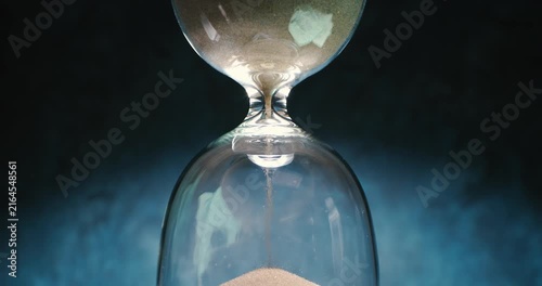 Hourglass with flowing sand on dark background.Shot on super slow motion camer.
