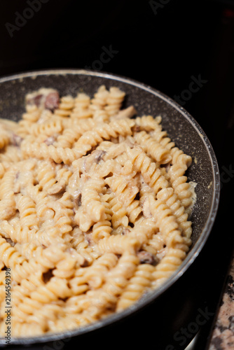 Fusilli pasta cooking in creamy mushroom sauce in pan.