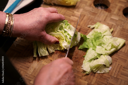 Cutting lettuce head with knife on wooden cutting board. Woman cutting fresh lettuce.