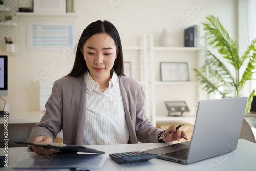 Asian businesswoman calculating expenses while reviewing financial documents at her desk.