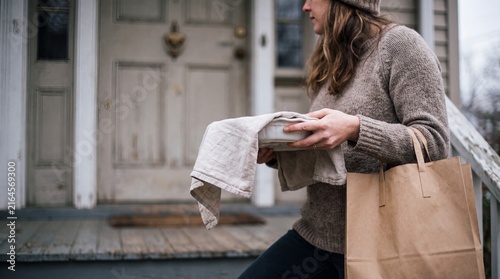 Woman delivering takeout food and grocery bag to a home front porch