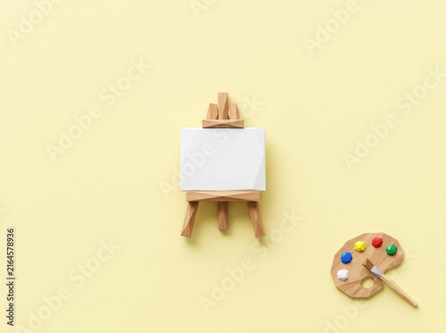 Miniature wooden easel and colorful art palette on yellow.