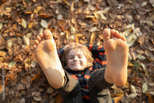Canvastavla happy boy of about ten lies on the ground, which is strewn with fallen leaves, cheerfully kicking his bare feet up in the air