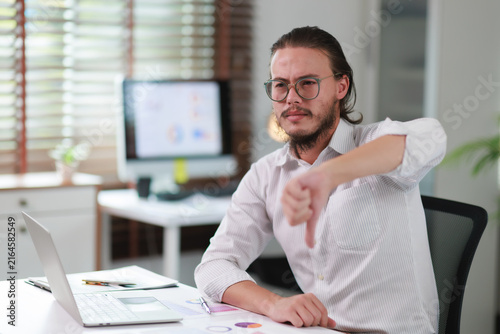Photography Young business person making thumbs down gesture at office desk, expressing diss