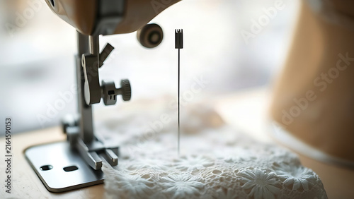 A threaded needle poised above delicate lace fabric on an old sewing machine.