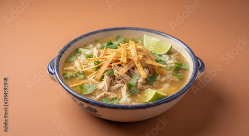 A clean, studio-lit commercial photograph of a single bowl of Sopa de Lima isolated against a solid warm-earth background,