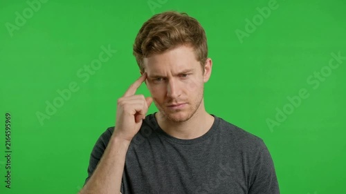 A young man thoughtfully contemplating with a neutral expression against a bright green background