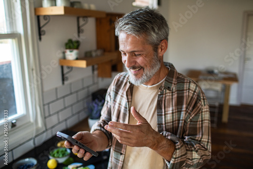 Smiling middle-aged man on video call with smartphone in home kitchen