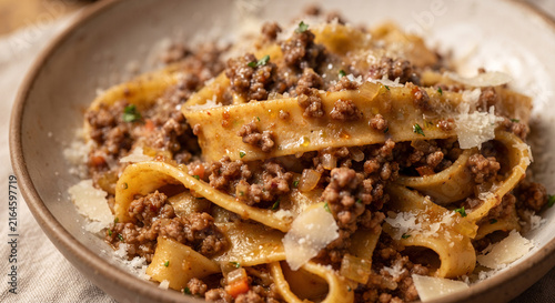 A vibrant, close-up photograph of golden, hand-rolled tagliatelle ribbons generously coated in a rich, slow-simmered, textured meat ragù, finished with a heavy grating of Parmigiano-Reggiano cheese.