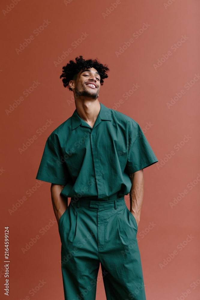 Obraz premium Standing full body young man in coordinated green outfit on terracotta backdrop for vertical poster and editorial fashion background