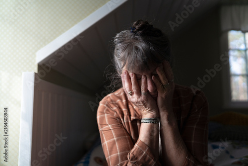 Mature woman sitting with hands covering face in bedroom at home