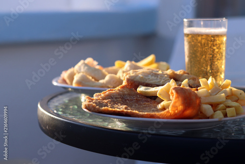 Foto Delicious fish with fries on a plate and two glasses of light beer on a glass table