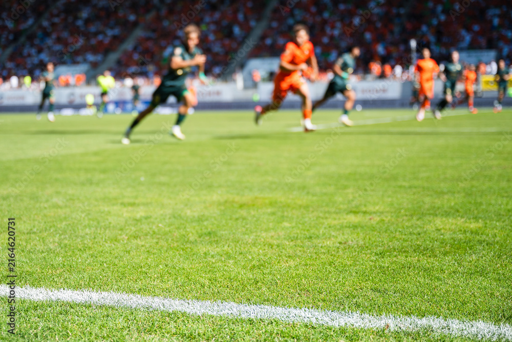 Fototapeta premium Professional soccer field with green grass and blurred stadium crowd under bright floodlights, creating a dynamic background for football and sports concepts.