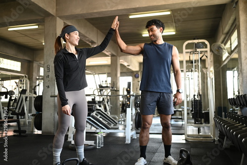 Happy diverse fitness couple sitting on a modern gym floor smiling and talking together while resting after an intense kettlebell strength training workout to promote an active lifestyle.