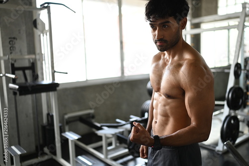 Photography Focused muscular Asian male athlete with a sweaty bare torso standing inside a modern gym facility showing intense dedication during a heavy bodybuilding strength training workout routine