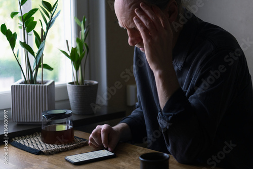 Depressed senior man using smart phone at home