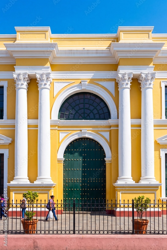 Fototapeta premium Colorful facade of a historic yellow colonial building featuring white columns and a grand green arched door