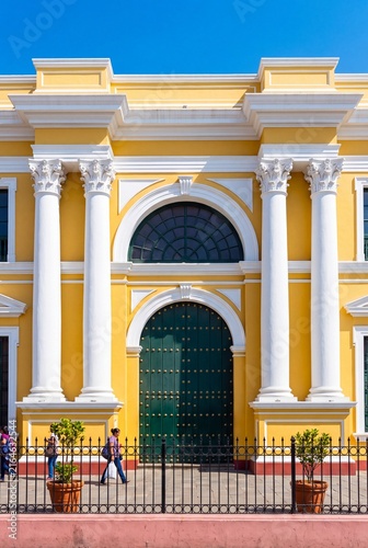 Colorful facade of a historic yellow colonial building featuring white columns and a grand green arched door
