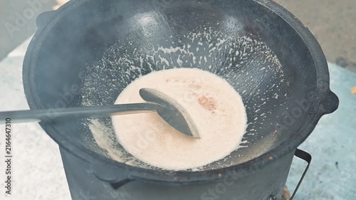 A cook stirs a creamy mixture in a pot on the stove as steam rises from the heat.
