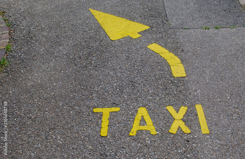 Yellow taxi road sign with curved arrow painted on asphalt pavement