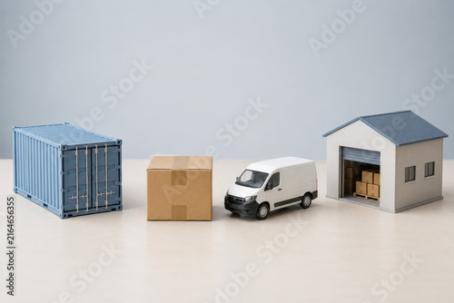 Miniature model of a blue shipping container, cardboard box, delivery van, and storage building with visible boxes inside on a light background