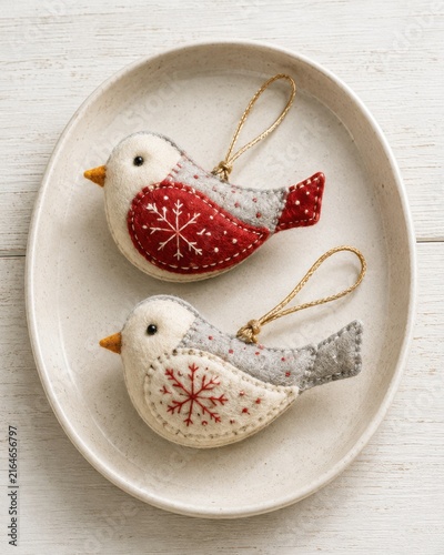 Decorative felt bird ornaments in red and white colors with snowflake patterns displayed on a round ceramic plate against a light wooden background
