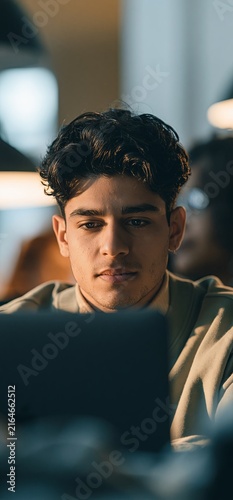 Young man concentrating on bright laptop screen in dark room. Young man working late, eyes reflecting blue light from a digital screen