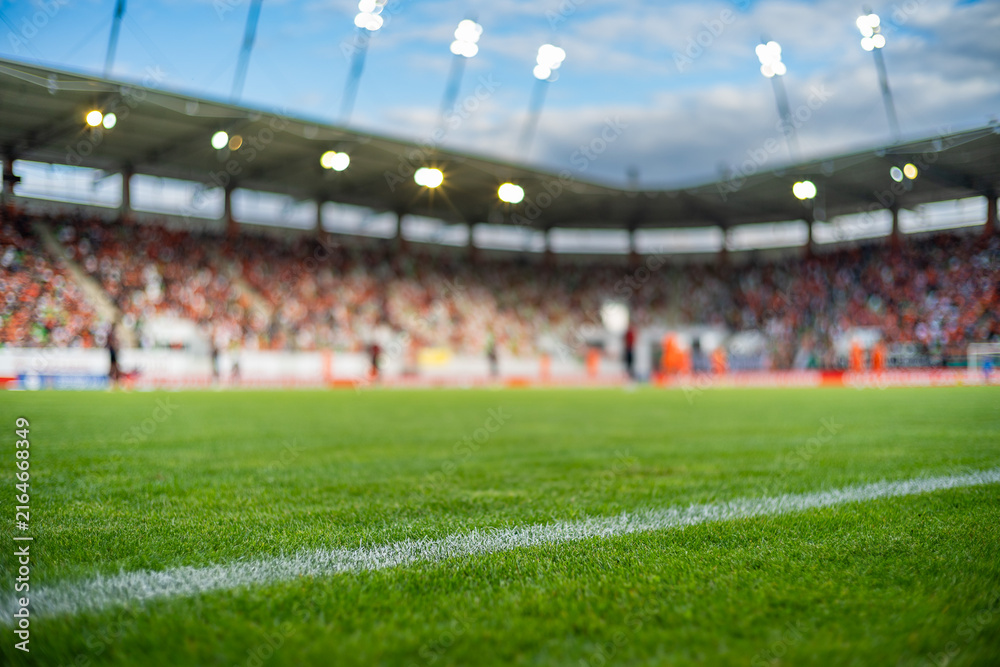 Fototapeta premium Professional soccer field with green grass and blurred stadium crowd under bright floodlights, creating a dynamic background for football and sports concepts.
