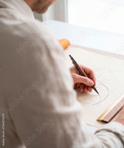 Architect or designer sketching geometric golden ratio diagram with mechanical pencil on drafting paper at desk