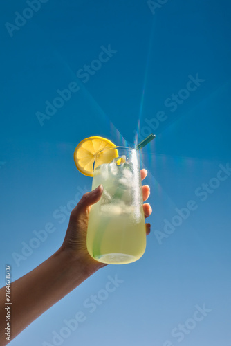 A hand holds a glass of refreshing lemonade over blue sky