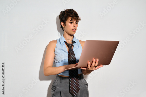 Professional woman using laptop. A woman in a blue shirt and tie holds a laptop. She looks focused, typing or reviewing content. Her expression