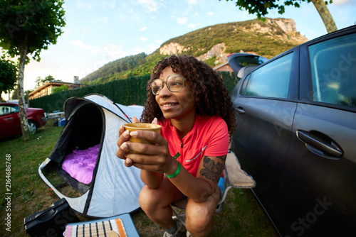 Woman enjoying coffee at campsite with tent and car