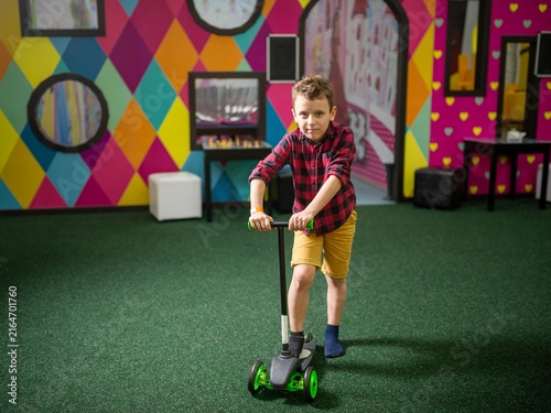 Canvas Print Boy riding a green kick scooter indoors