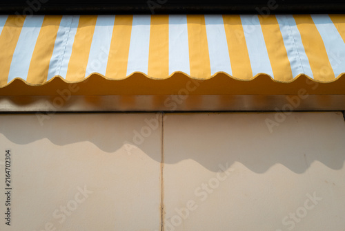 Close-up of yellow-white striped awning shading beige building wall