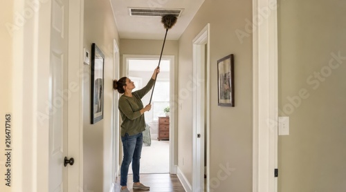 Apartment resident dusting ceiling ventilation grille in hallway
