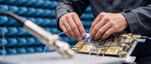 Electronics technician testing circuit board prototype in RF lab with hands-on microelectronics work