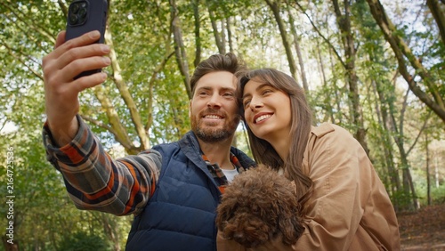 Konstfotografi Caucasian couple taking selfie outdoors smiling warmly while woman holding small brown dog