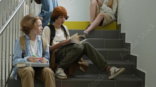 Caucasian teenagers sitting on school stairs, discussing homework and writing in notebook. Footage is perfect for educational marketing, school enrollment campaigns, and student lifestyle promos