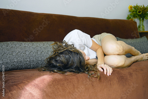 Obraz na płótnie Exhausted woman lying in fetal position on sofa, face completely hidden by curls