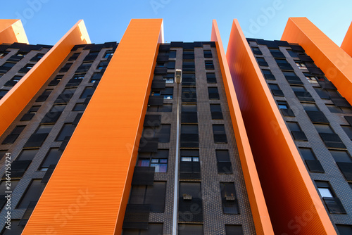 Foto Low-angle view of a modern high-rise building with dramatic orange vertical fins alternating with dark brick facade sections, rising against a clear blue sky