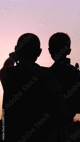 Father and son enjoy sunset together. Dad and child share special moment, creating lasting memories. Silhouette captures love and connection in vertical format. Happy family.