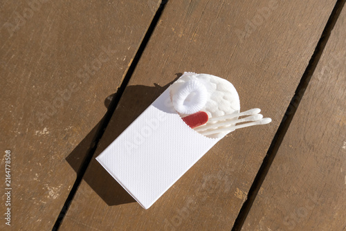 Hotel guest care kit with personal hygiene essentials. Cotton pads, cotton buds, hair band and nail file arranged in a small paper packet, representing hospitality service and travel essentials