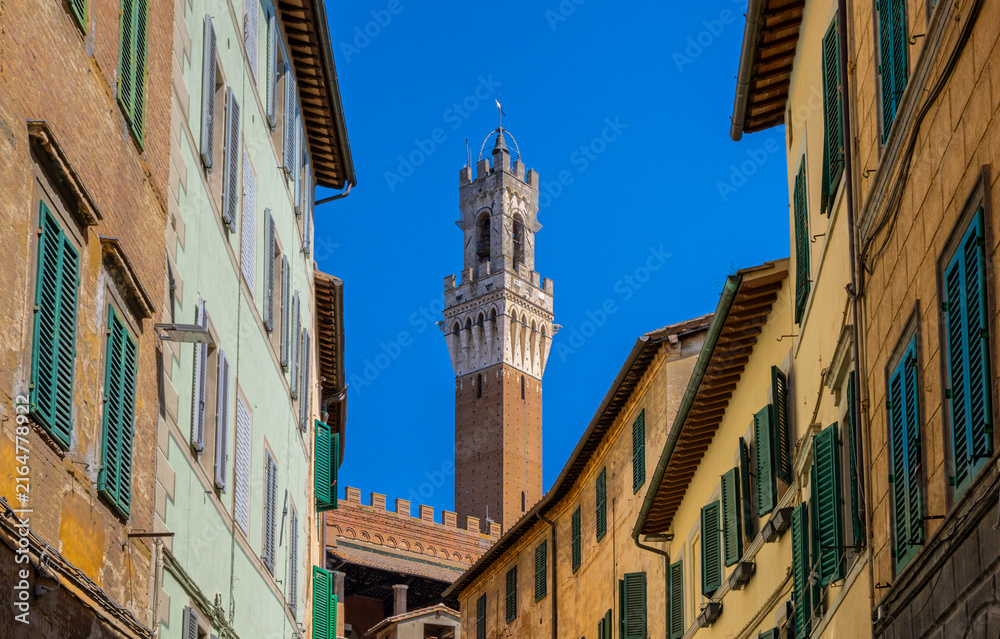 Naklejka premium Blick durch eine enge Gasse auf den Torre del Mangia, den markanten Glockenturm des Palazzo Pubblico in Siena, Toskana, Italien