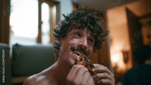 Cheerful Young Man Eating Chocolate Donut with Frosting Mustache