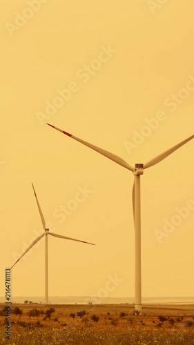 Wind turbines generate renewable energy in rural landscape. Vertical windmills stand tall against golden sky. Sustainable energy production promotes eco-friendly future.