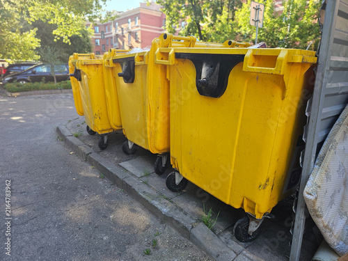 Four yellow trash bins lined up on a street outside