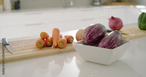 Camera is panning right and forward, revealing carrots with knife on white counter for display