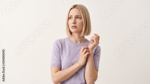 Thoughtful young blonde woman wearing a light purple sweater looking sideways with a concerned expression against a plain white background